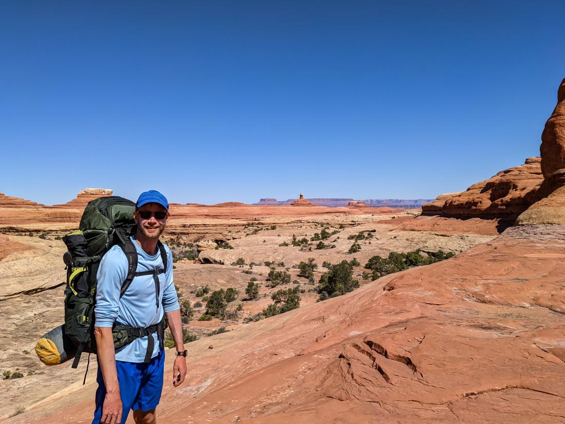 A man with hiking gear standing in front of a canyon.