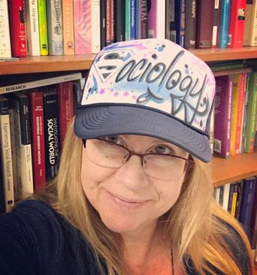 Smiling woman wearing a Sociology hat with books in the background