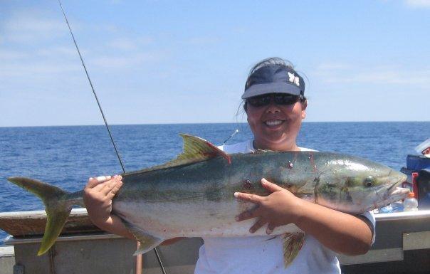 A woman in sunglasses holds a yellowfin tuna on a boat.