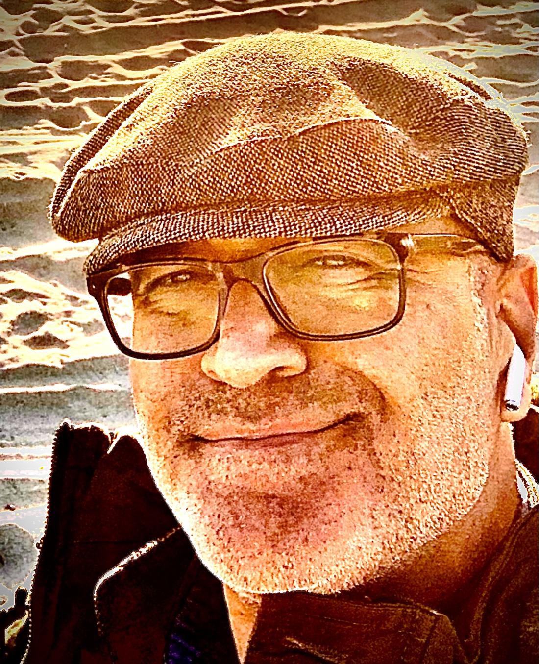 Man wearing glasses and a hat smiling 