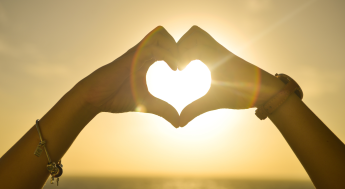 Sun rays coming though an opening of hands making a heart shape