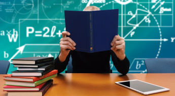 Person sitting at desk with book covering face and math symbols in background