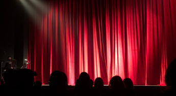 Audience looking at an empty stage with a closed red curtain