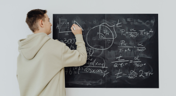 Male student in a sweatshirt doing math on a chalkboard