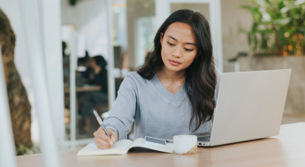 Female student writing in notebook next to a laptop