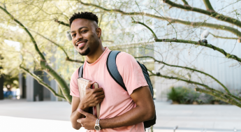 Black male student with backpack and books smiling