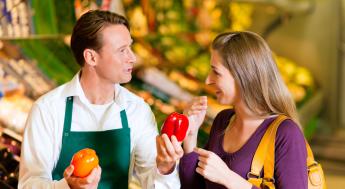 Grocery worker showing bell peppers to customer