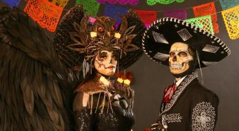 2 PEOPLE WEARING SKULL MAKE UP DRESSED IN TRADITIONAL MEXICAN CLOTHES FOR DAY OF THE DEAD. 