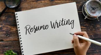 A note pad with Resume Writing written in calligraphy with a person's hand holding a fountain pen 