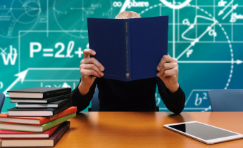 Person sitting at desk with book covering face and math symbols in background