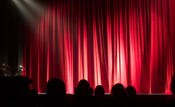 Audience looking at an empty stage with a closed red curtain