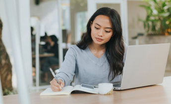 Female student writing in notebook next to a laptop