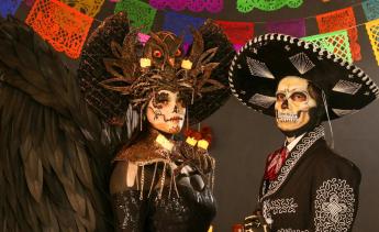 2 PEOPLE WEARING SKULL MAKE UP DRESSED IN TRADITIONAL MEXICAN CLOTHES FOR DAY OF THE DEAD.