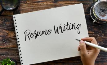 A note pad with Resume Writing written in calligraphy with a person's hand holding a fountain pen 