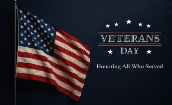 United States flag waving in the air. With the words "Veterans Day, Honoring All Who Served" on the right hand side.