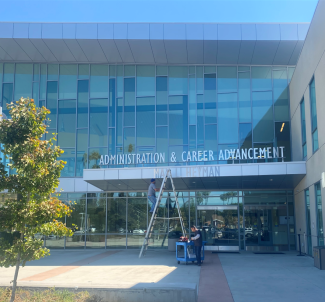 Front of Administration and Career Advancement building with two workers repairing sign. 