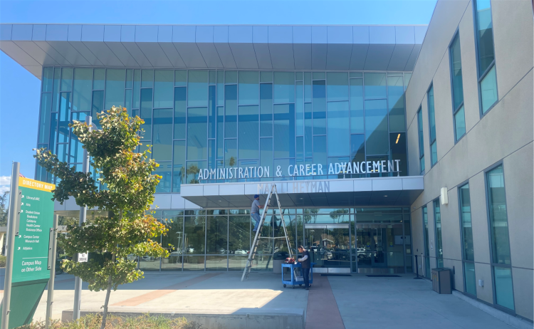 Front of Administration and Career Advancement building with two workers repairing sign. 