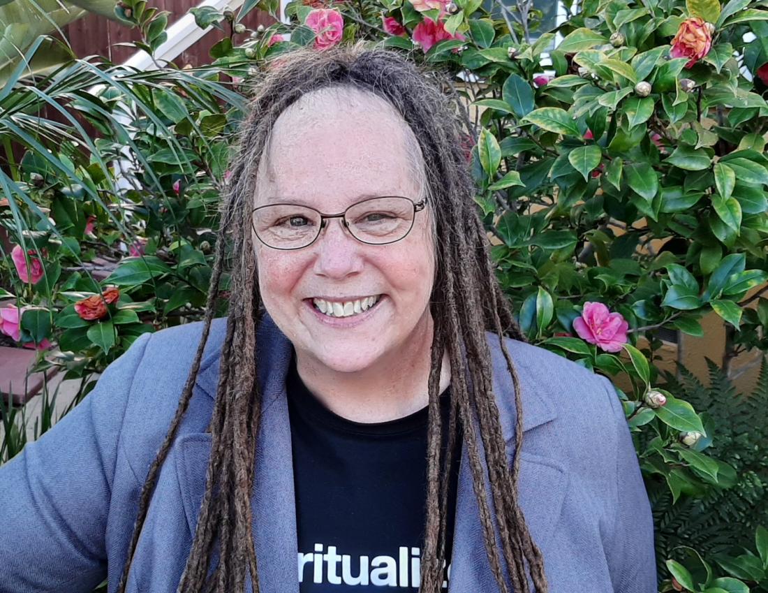 Woman smiling in t-shirt and blazer in front of background of flowers