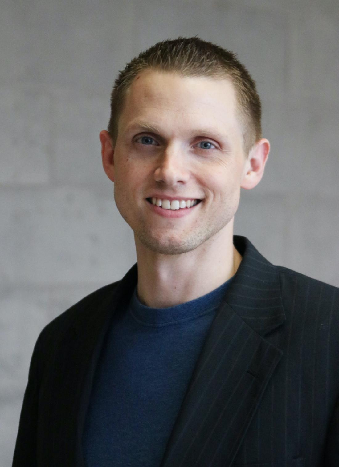 Smiling man in t-shirt and blazer in front of blank background. 