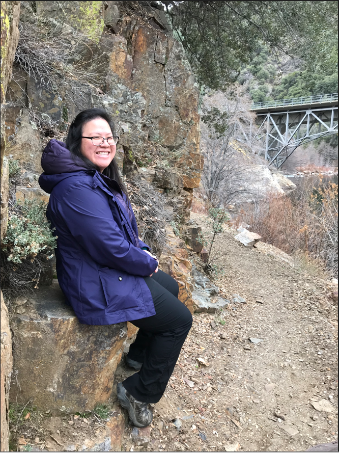 A woman sits next to a hiking trail.