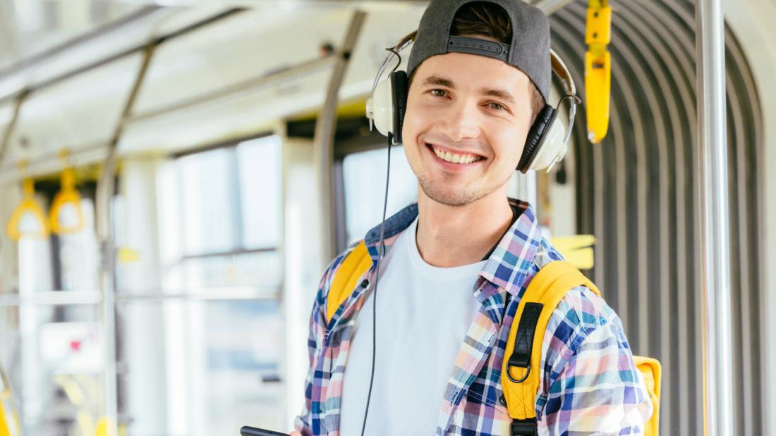 Male student with backpack and headphones riding the bus