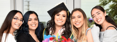 Female graduate holding flowers surrounded by friends