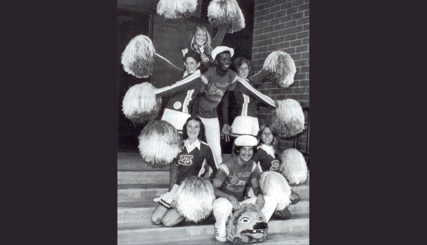 Man standing in the middle of LAVC Cheerleaders with pom poms in the 1970s